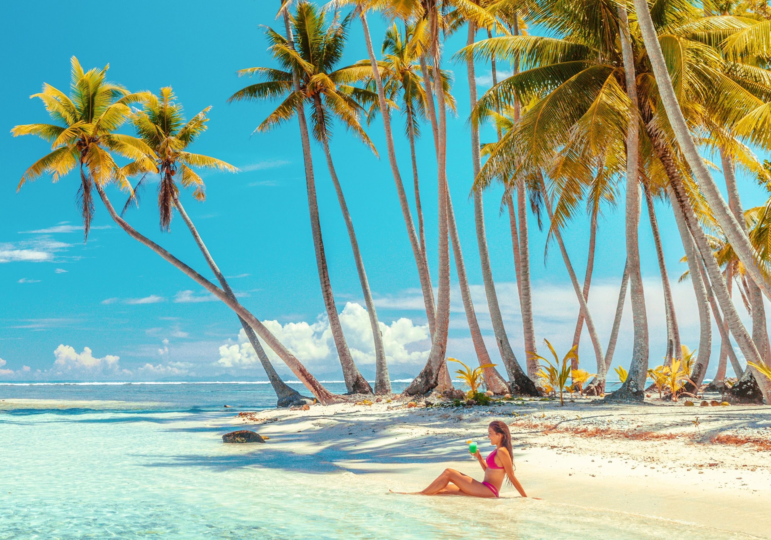 Woman enjoys drink, sun, beach vibe. Good for Maldives vacation search.
