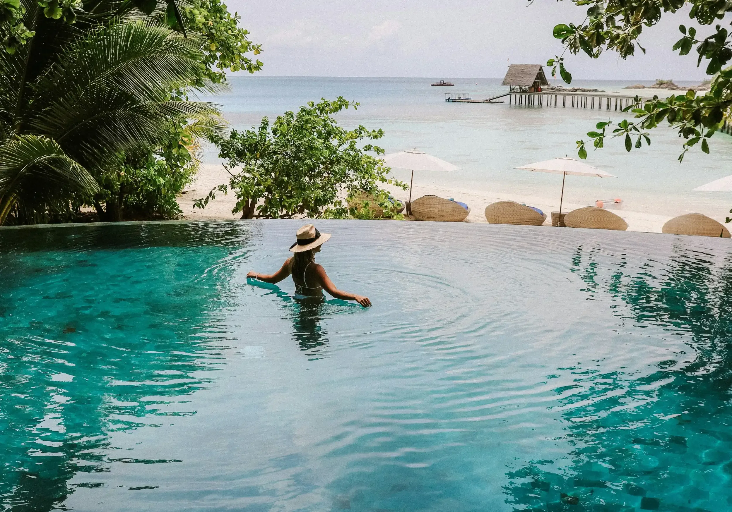 Woman enjoys Maldives tour, relaxing in infinity pool overlooking beach and ocean.