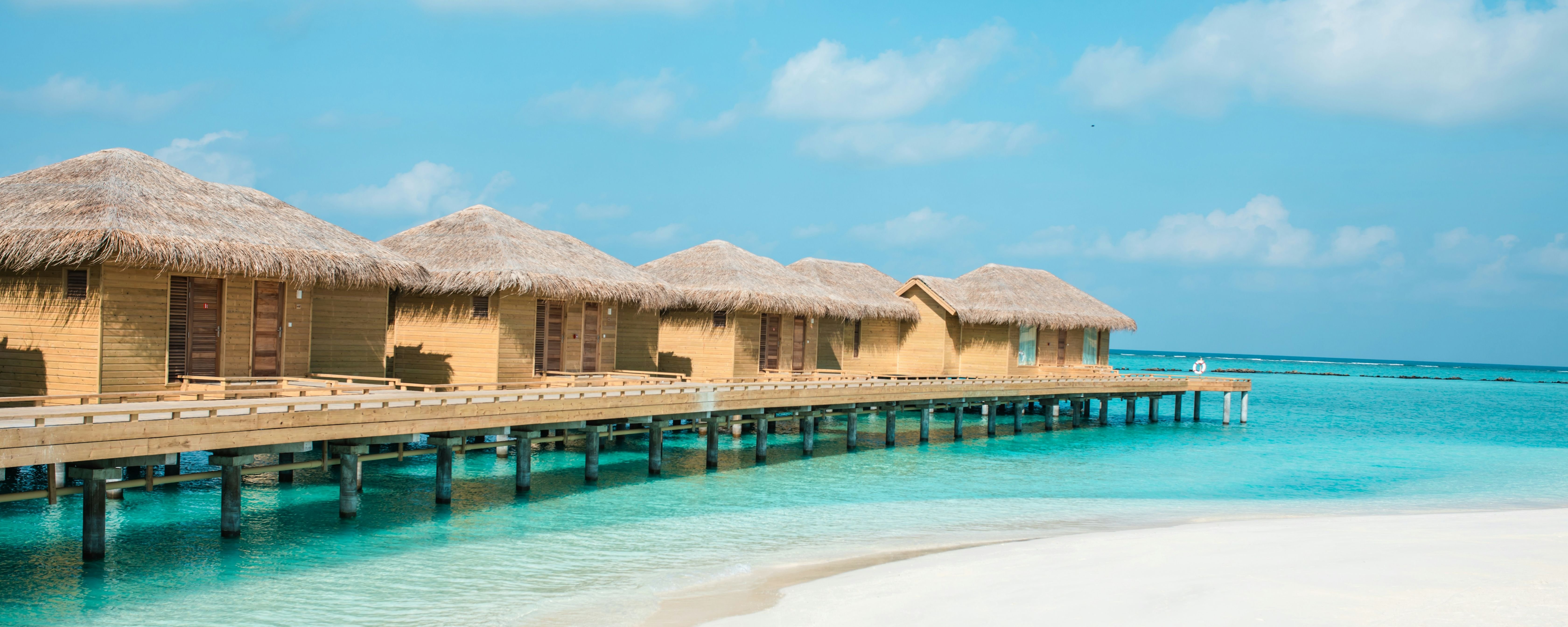 Wooden huts over blue water, bright sun. Nice Maldives tour spot.