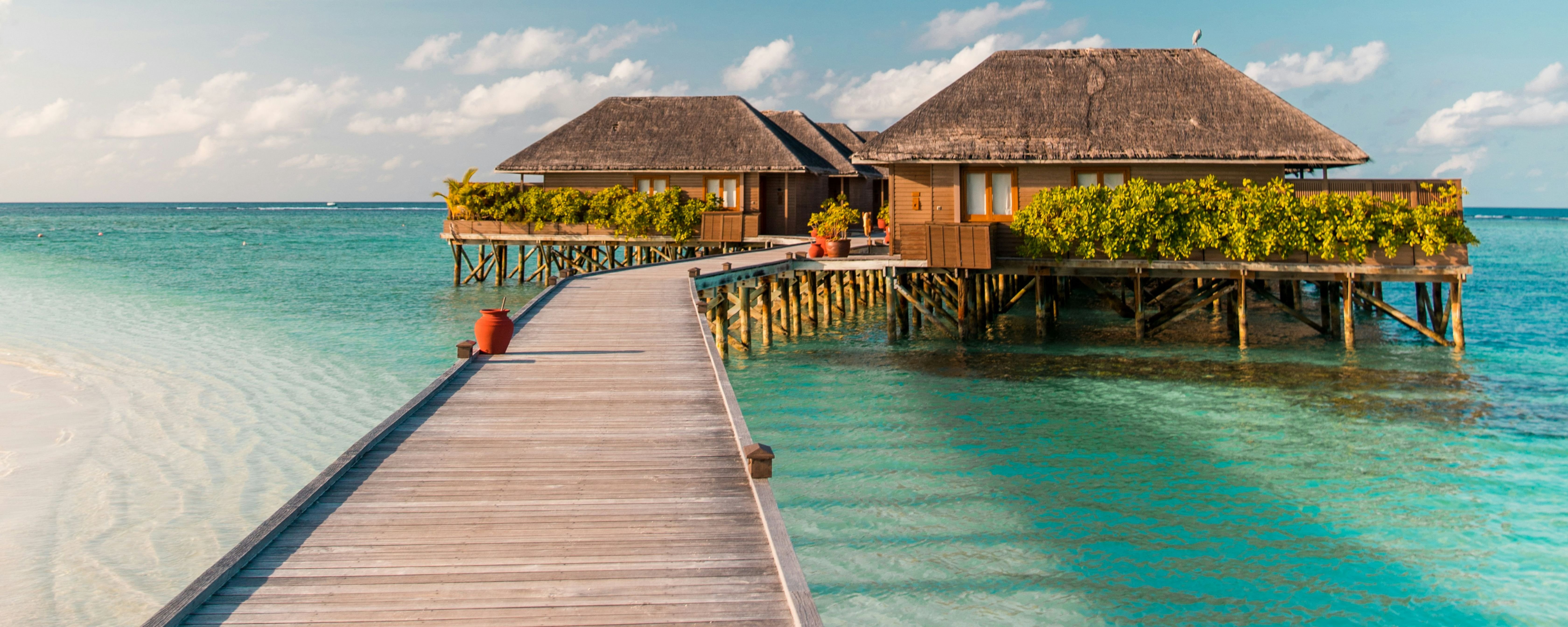 Beautiful view of Maldives Island during a Maldives tour. Wooden walkway leads to overwater bungalows on a clear day.
