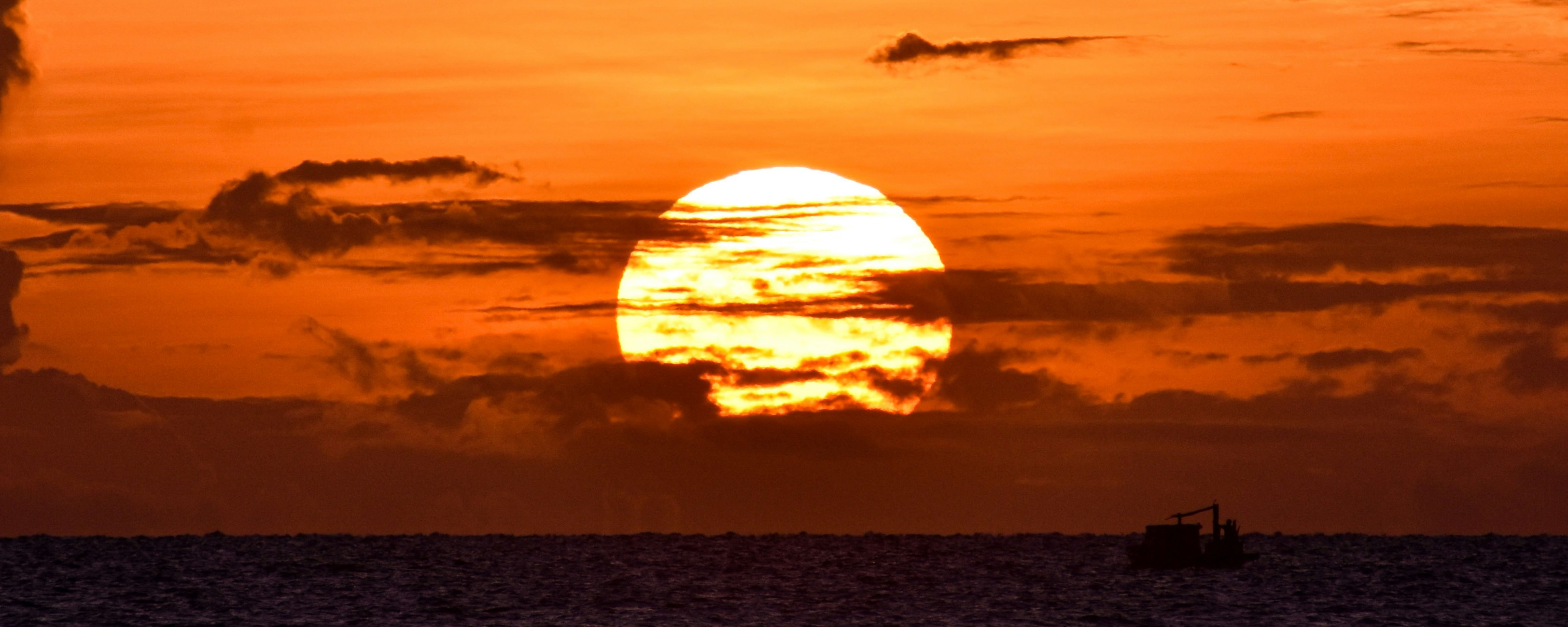 Sunset picture, Maldives tour boat. Beautiful ocean view. Sky orange, clouds soft. Good for travel blogs about Maldives trips.