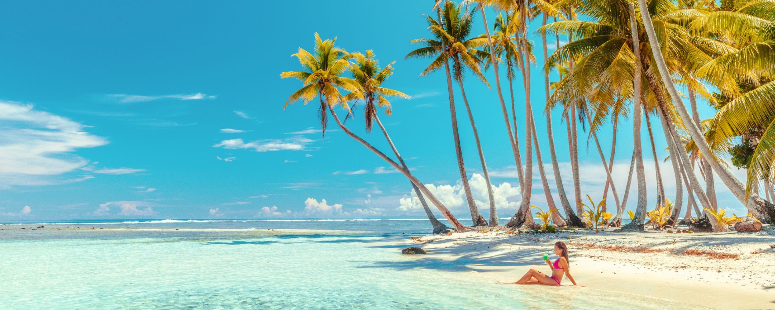 Woman sits on white sand beach near blue water and palm trees. Perfect for a Maldives tour!