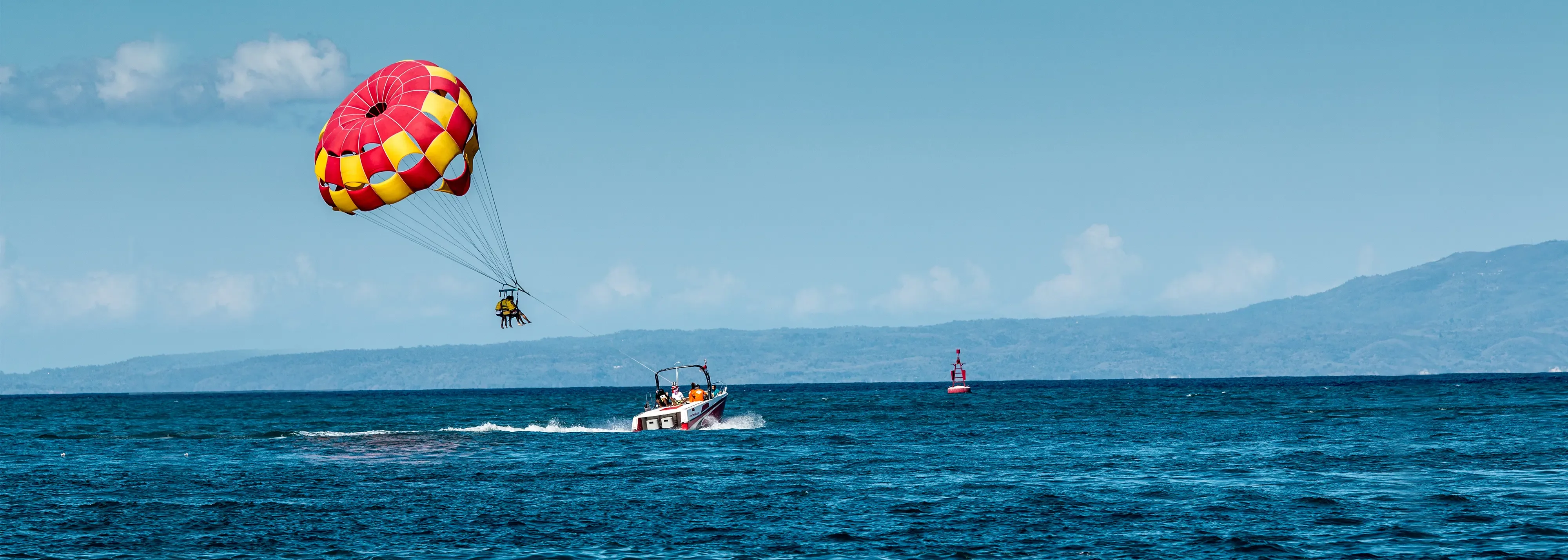 Exciting Bali tour activity: parasailing. People fly high above ocean with boat. Bright parasail.